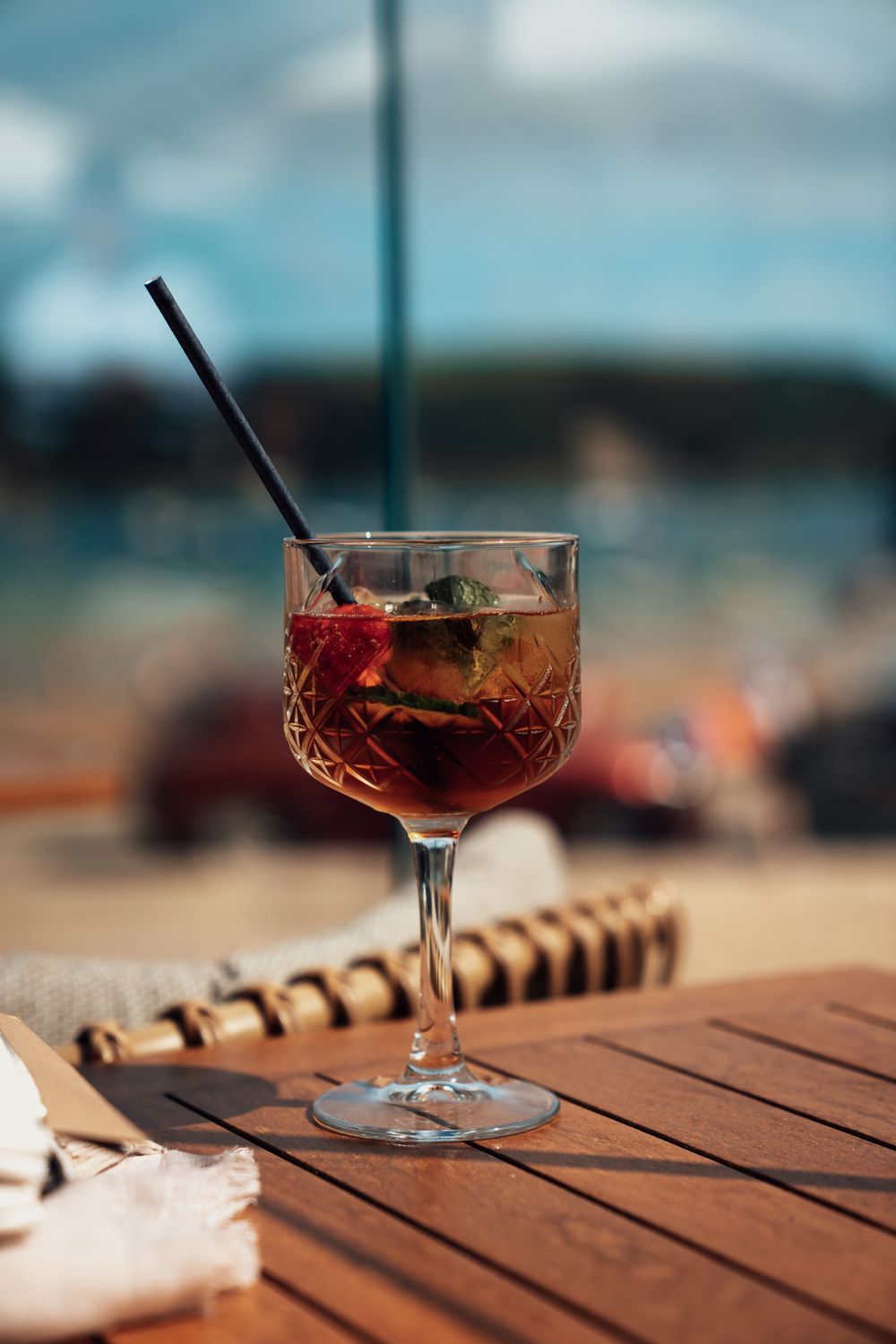 Elegant cocktail with red garnish served in a cut crystal glass on wooden table.