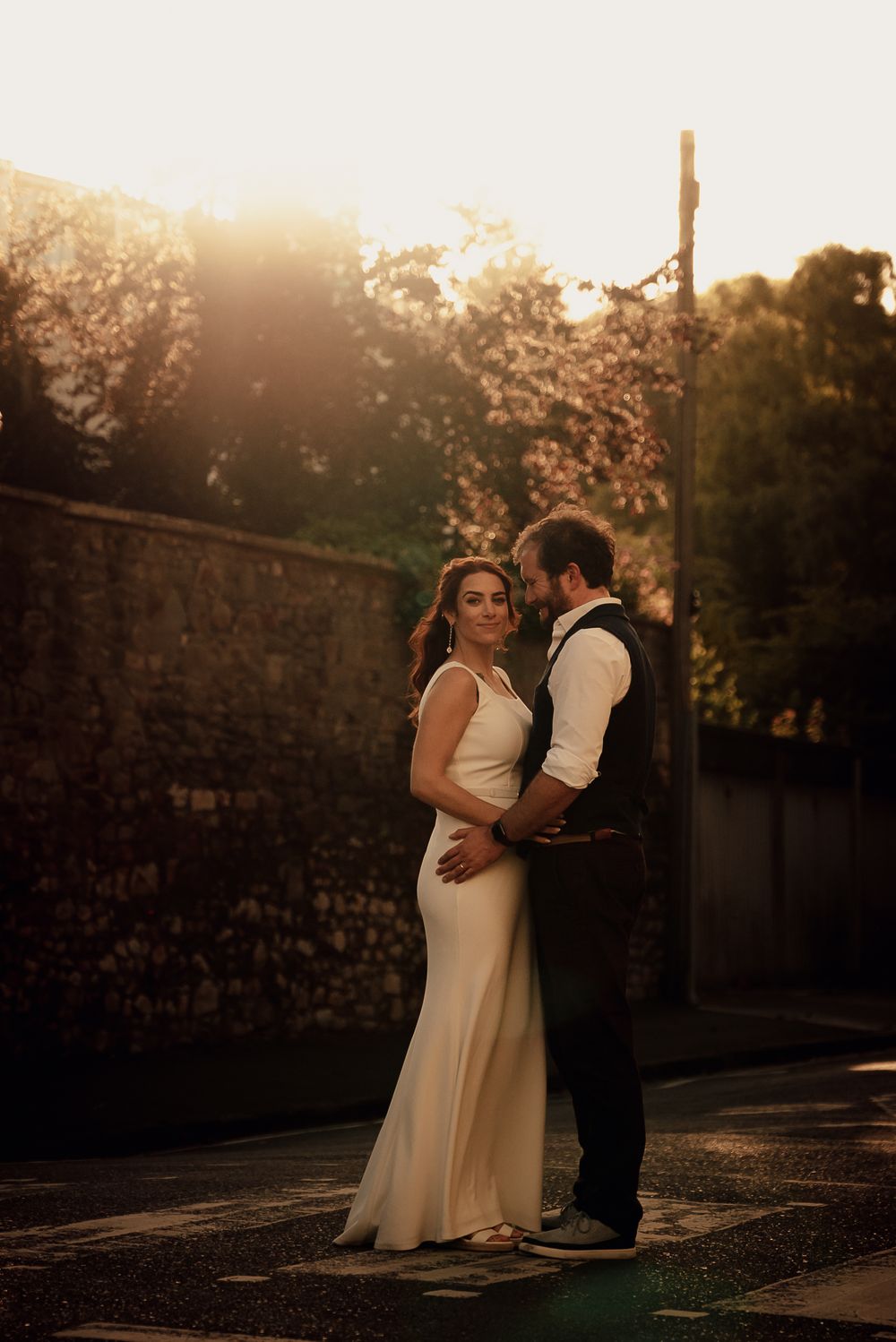 Wedding couple dancing together during golden hour against a stone wall backdrop.