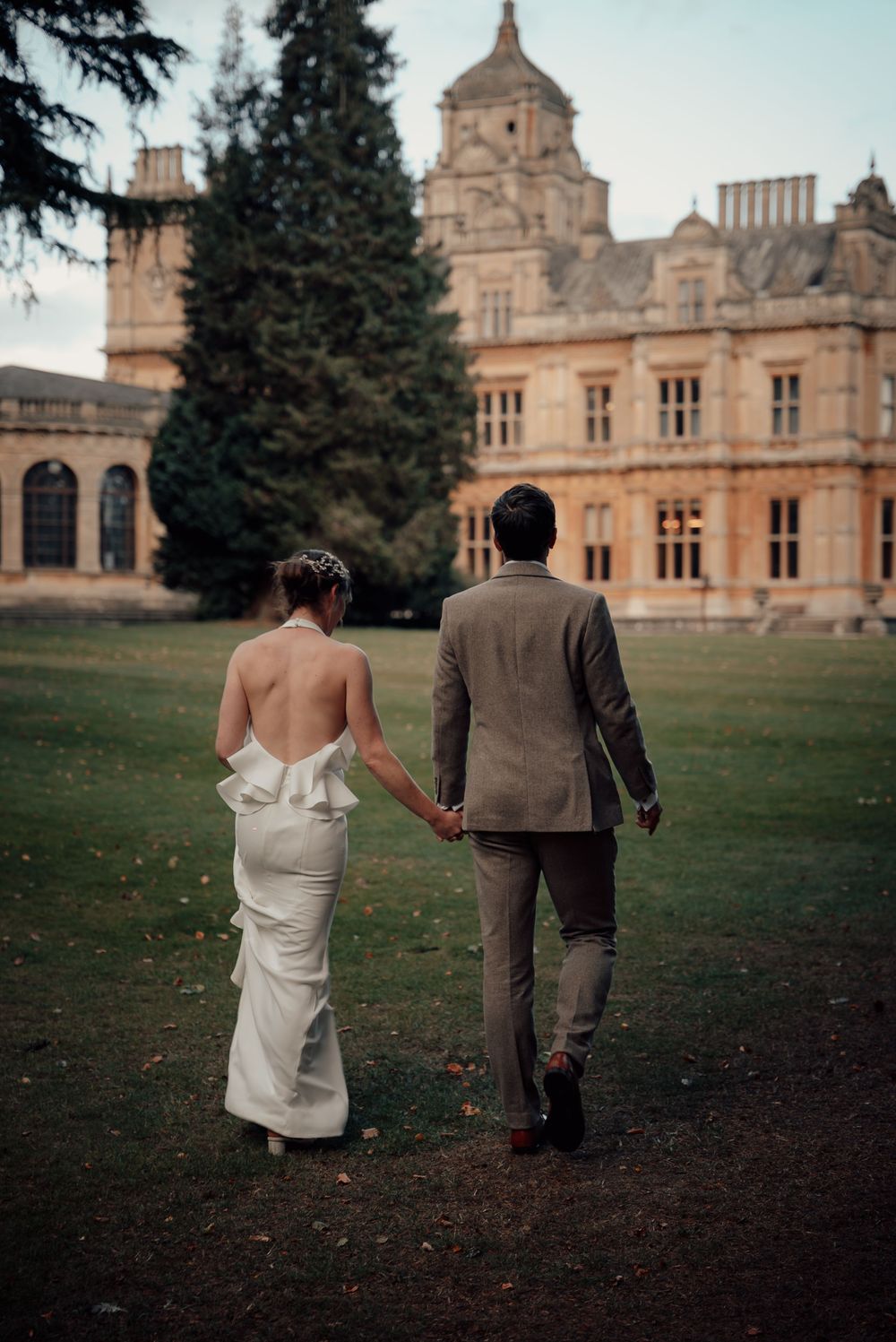A couple walks away from a grand historic mansion across a manicured lawn.