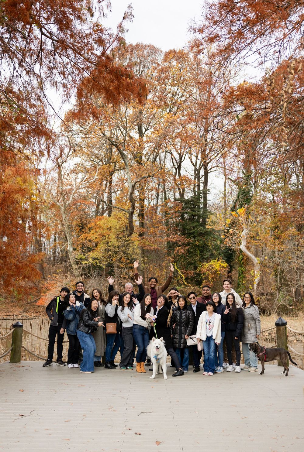 Large group of people gathered outdoors against a backdrop of autumn trees with orange and yellow foliage.