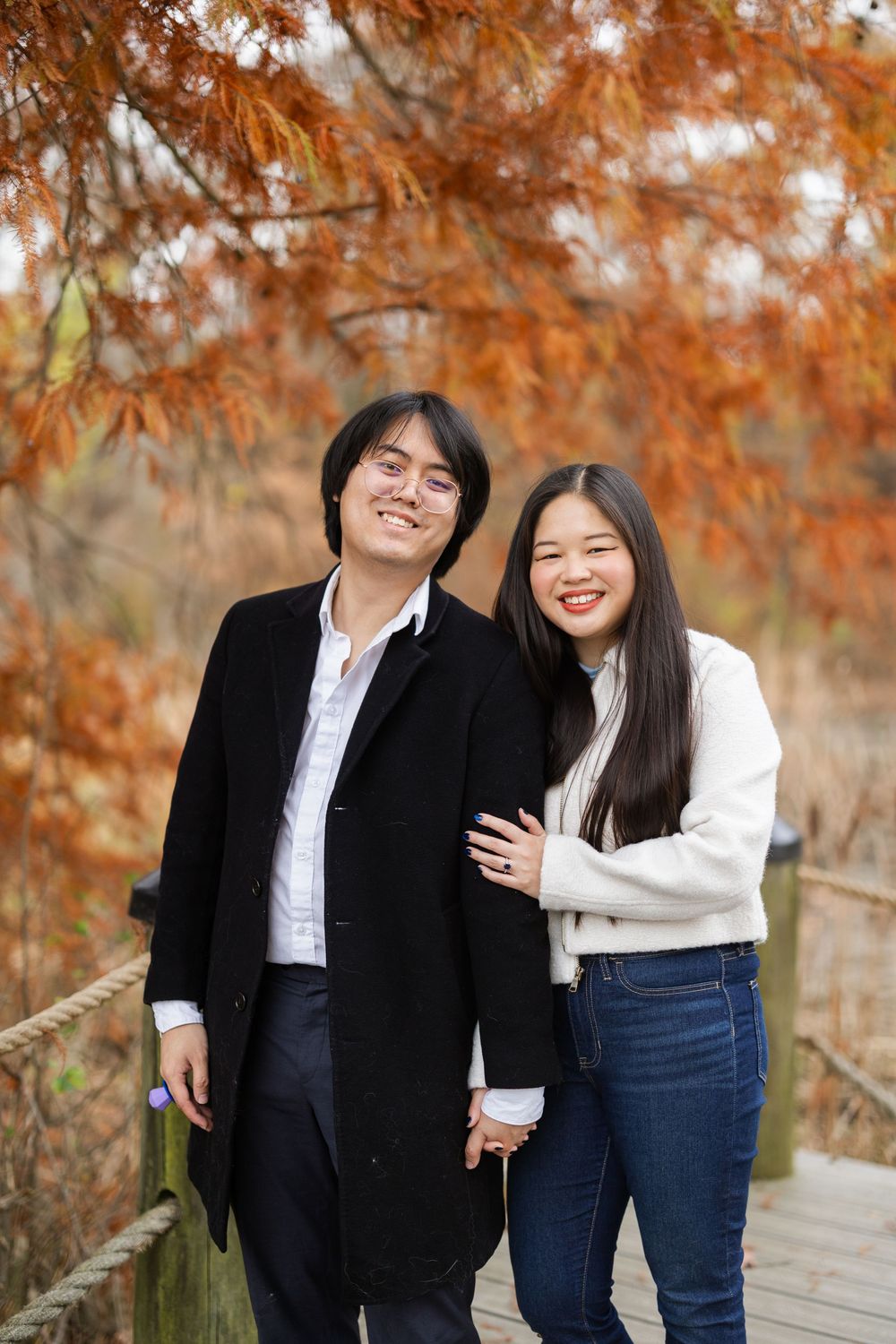 Two people in contrasting black and white outfits pose together against vibrant fall foliage.