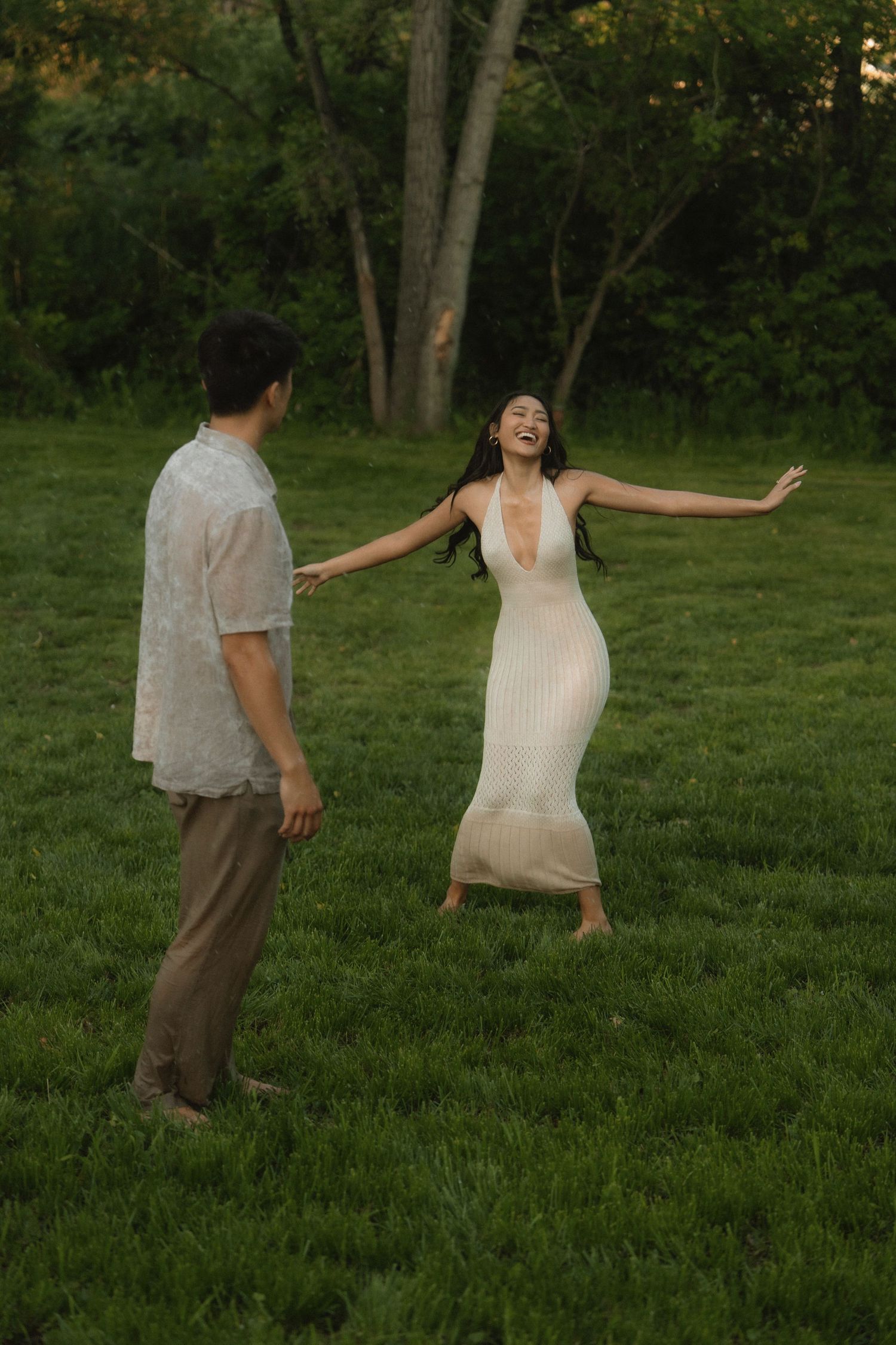 Romantic couple lying in tall grass field wearing white and earth-toned clothing.