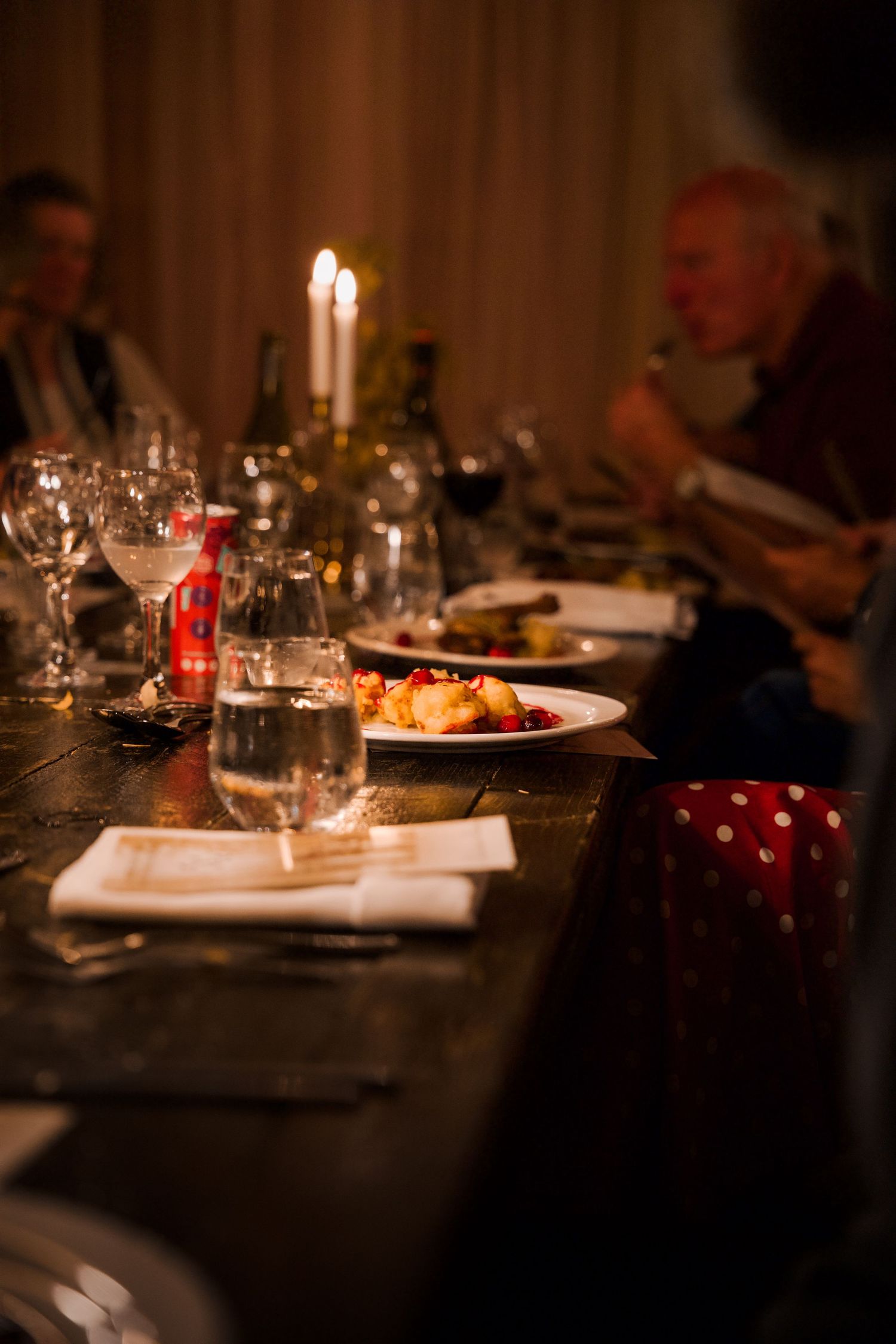 Intimate dinner table settings with glowing candles and white plates in low light.