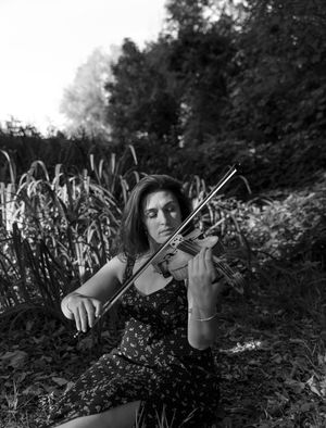 a black and white photo of a woman sitting in a field playing her violin.
