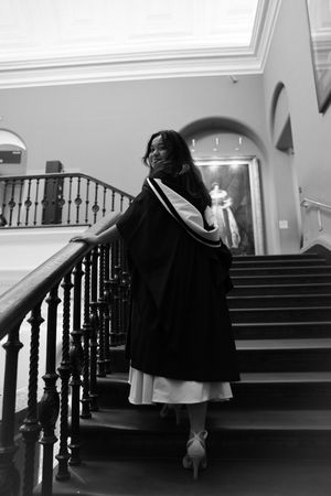 black and white photo of a girl in a graduation gown as she climbs the stairs at the v&a.
