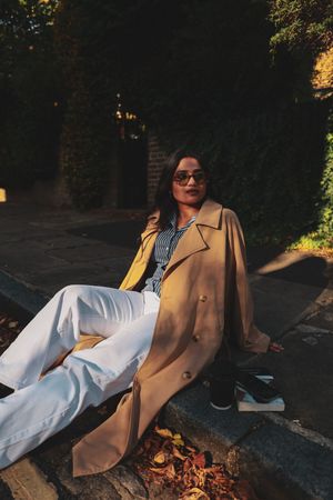 a photo of a woman in a trench coat posing while sitting on the pavement.