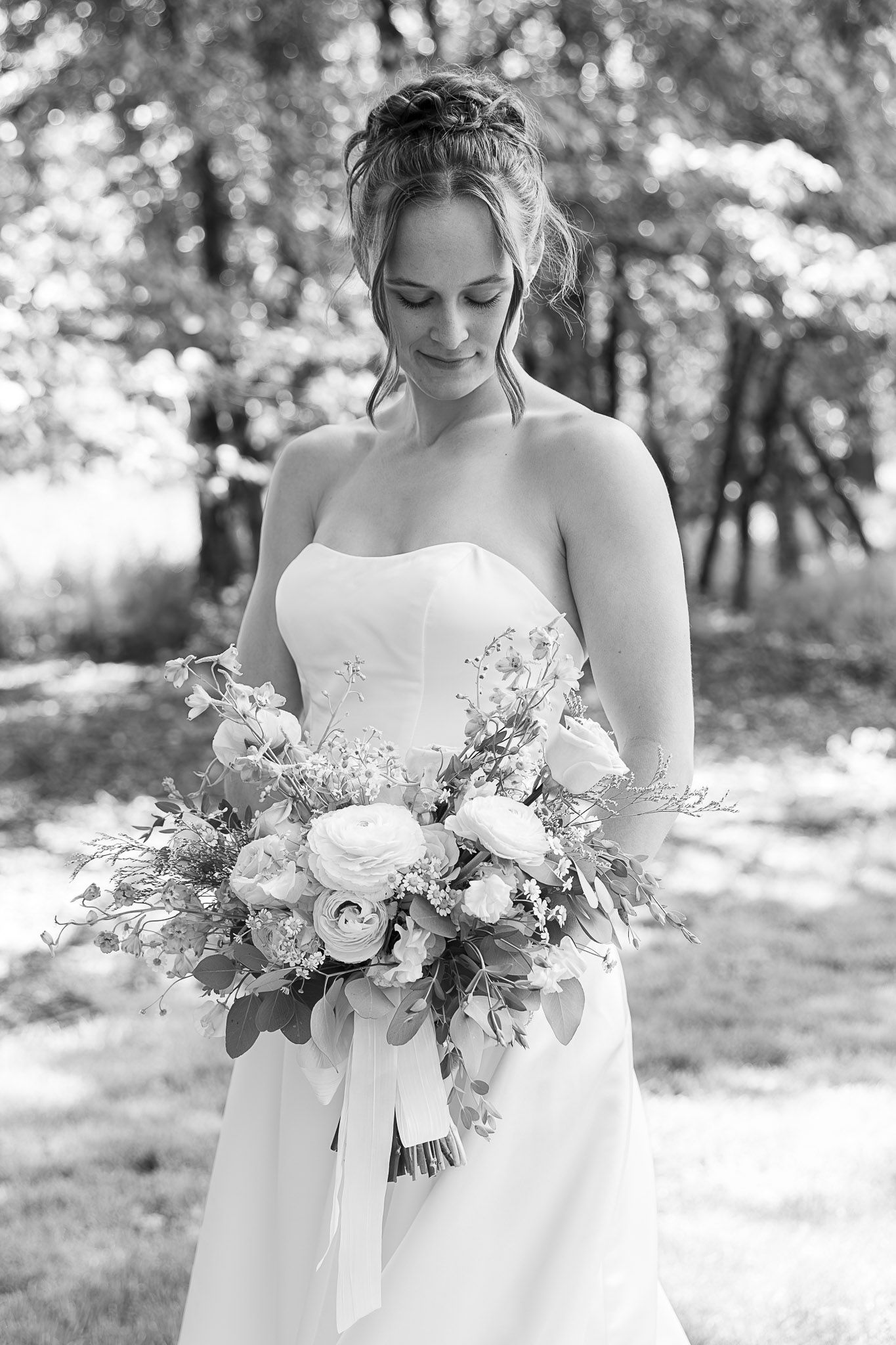 Black and white photo of a bride in a strapless gown holding a lush floral bouquet outdoors.
