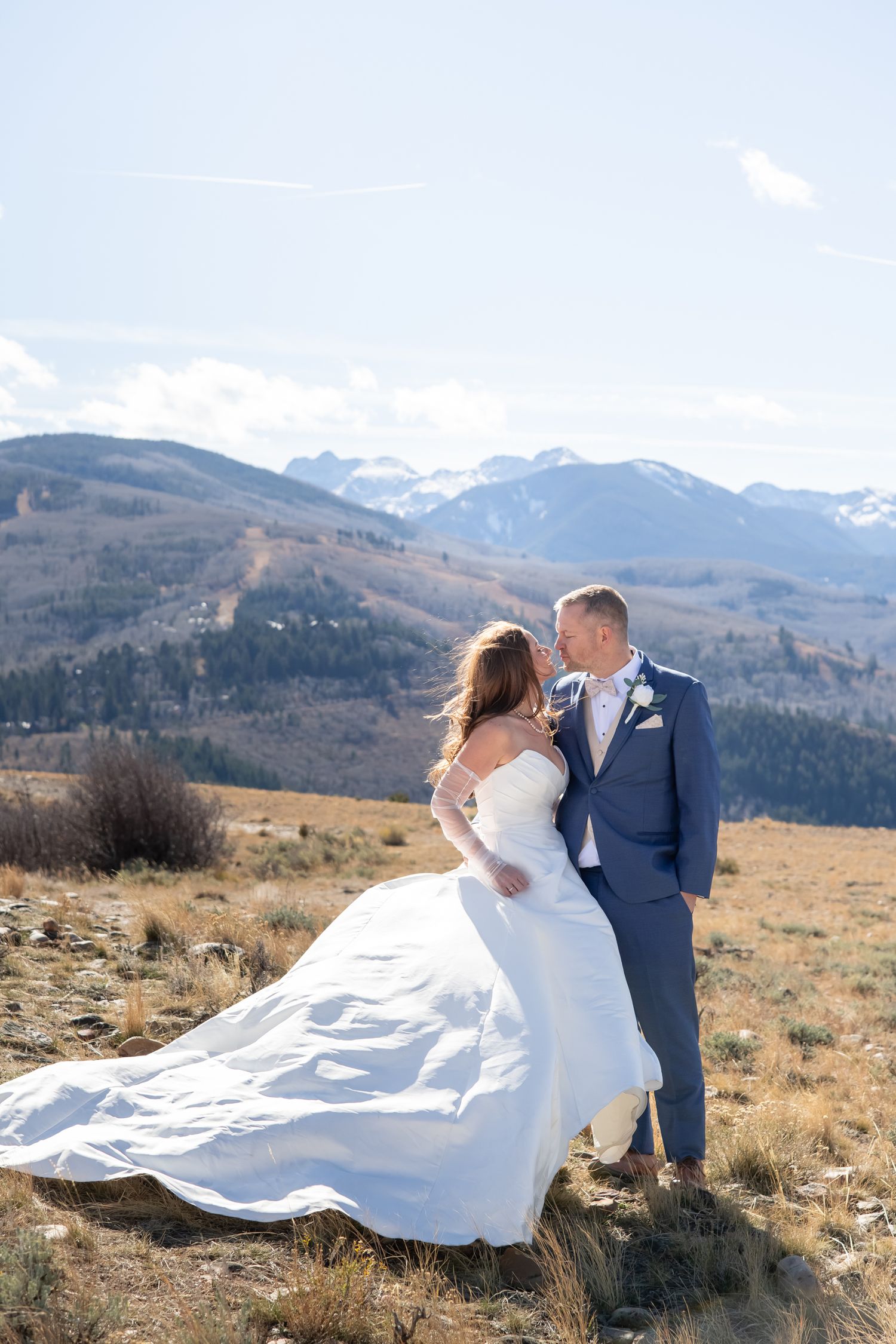Couple embraces on mountain summit with snow-capped peaks and dramatic mountain landscape in background during wedding in Beaver Creek CO