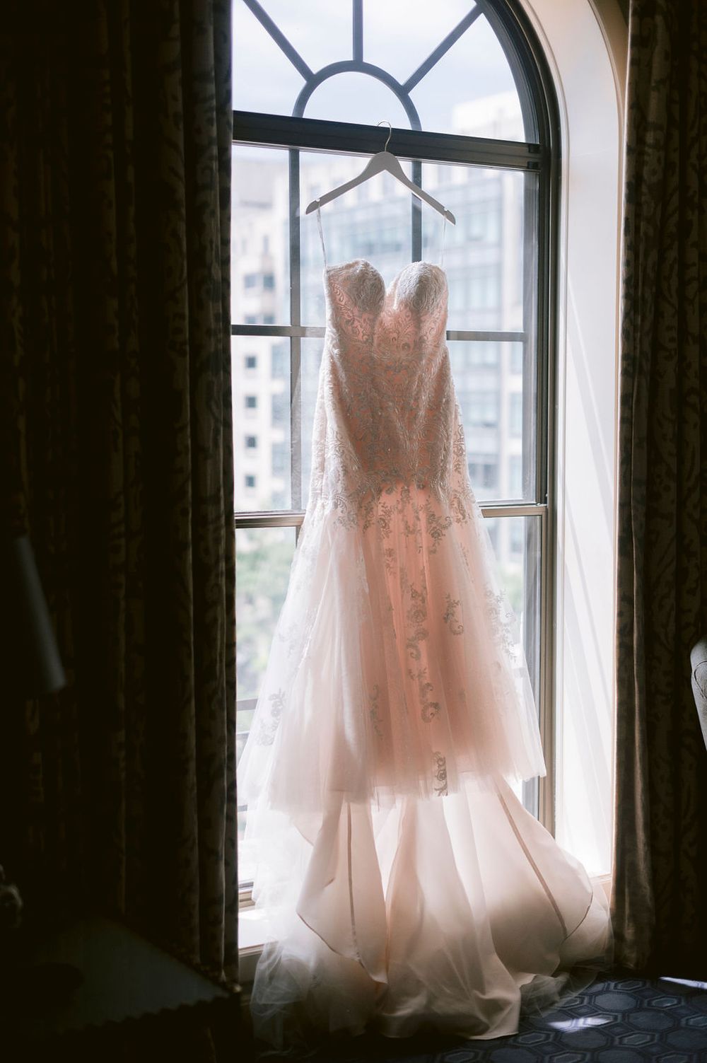 Wedding dress silhouetted against arched windows in natural light.