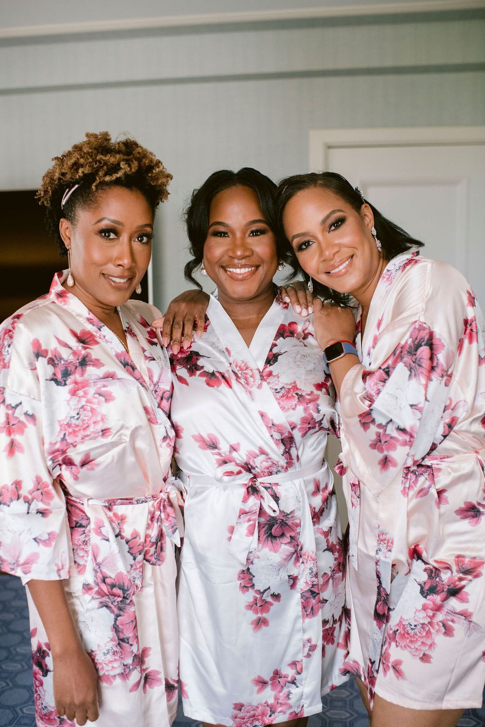 Bridesmaids wearing matching pink floral robes pose together before the wedding.