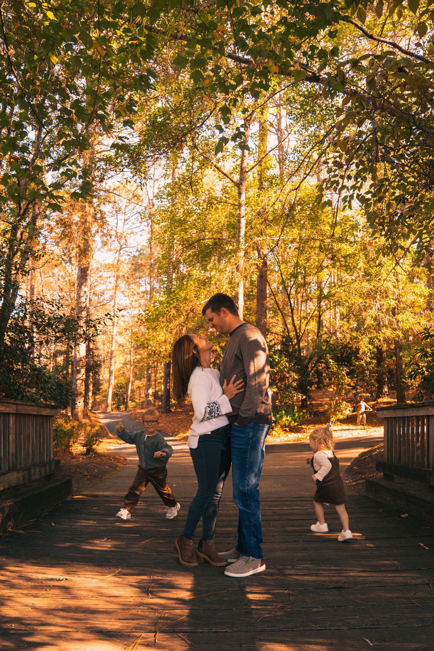 Family enjoying a golden autumn afternoon together on a wooden bridge surrounded by fall foliage.