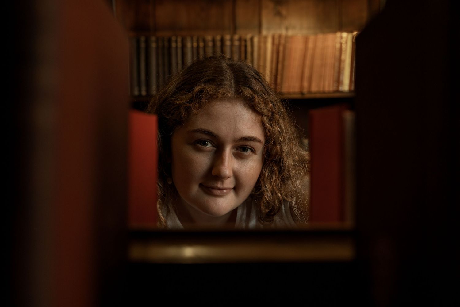 Dimly lit scene in a library with bookshelves creating dramatic shadows. Artistic Portrait Photography