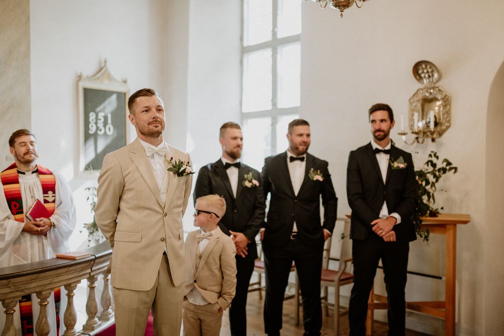 Brudgum står och väntar på bruden under en vigsel i Sandseryds kyrka, Jönköping. Brudgummen har beige kostym.