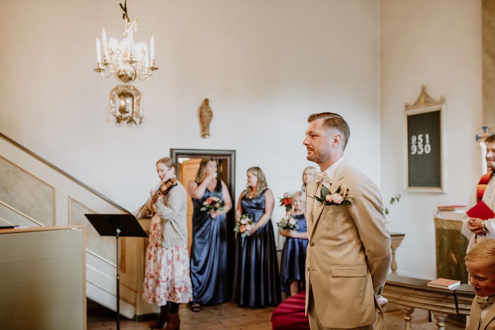 Brudgum och bestman står och väntar på bruden under en vigsel i Sandseryds kyrka, Jönköping. Brudgummen har beige kostym.