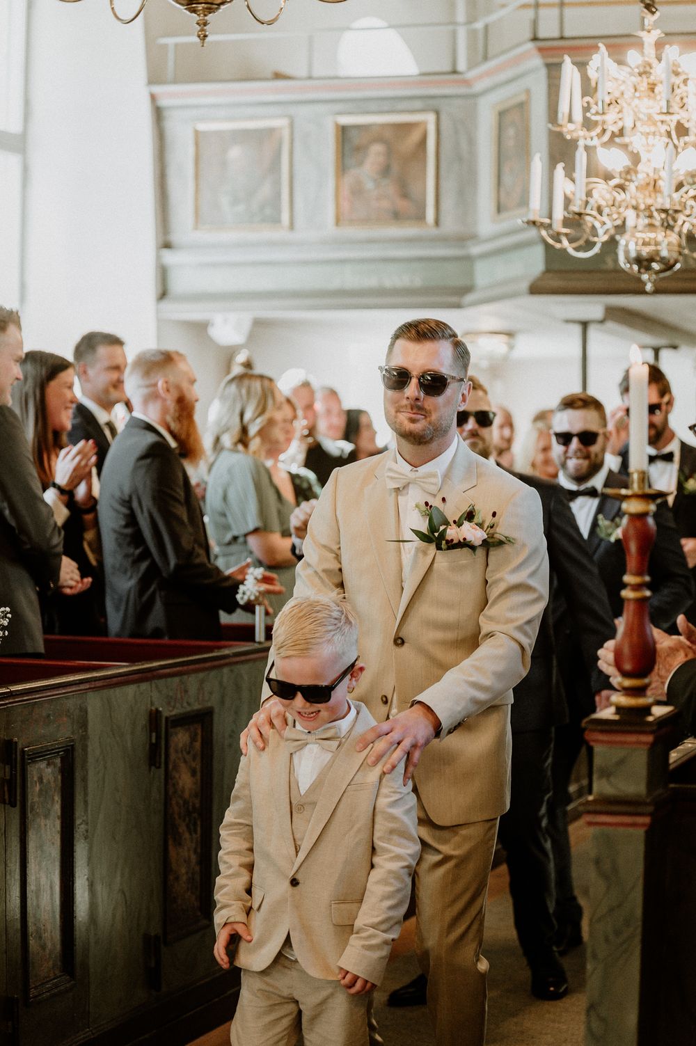 Brudgum och brudfölje går i altargången på Sandseryds kyrka under ett bröllop. Alla bär solglasögon.