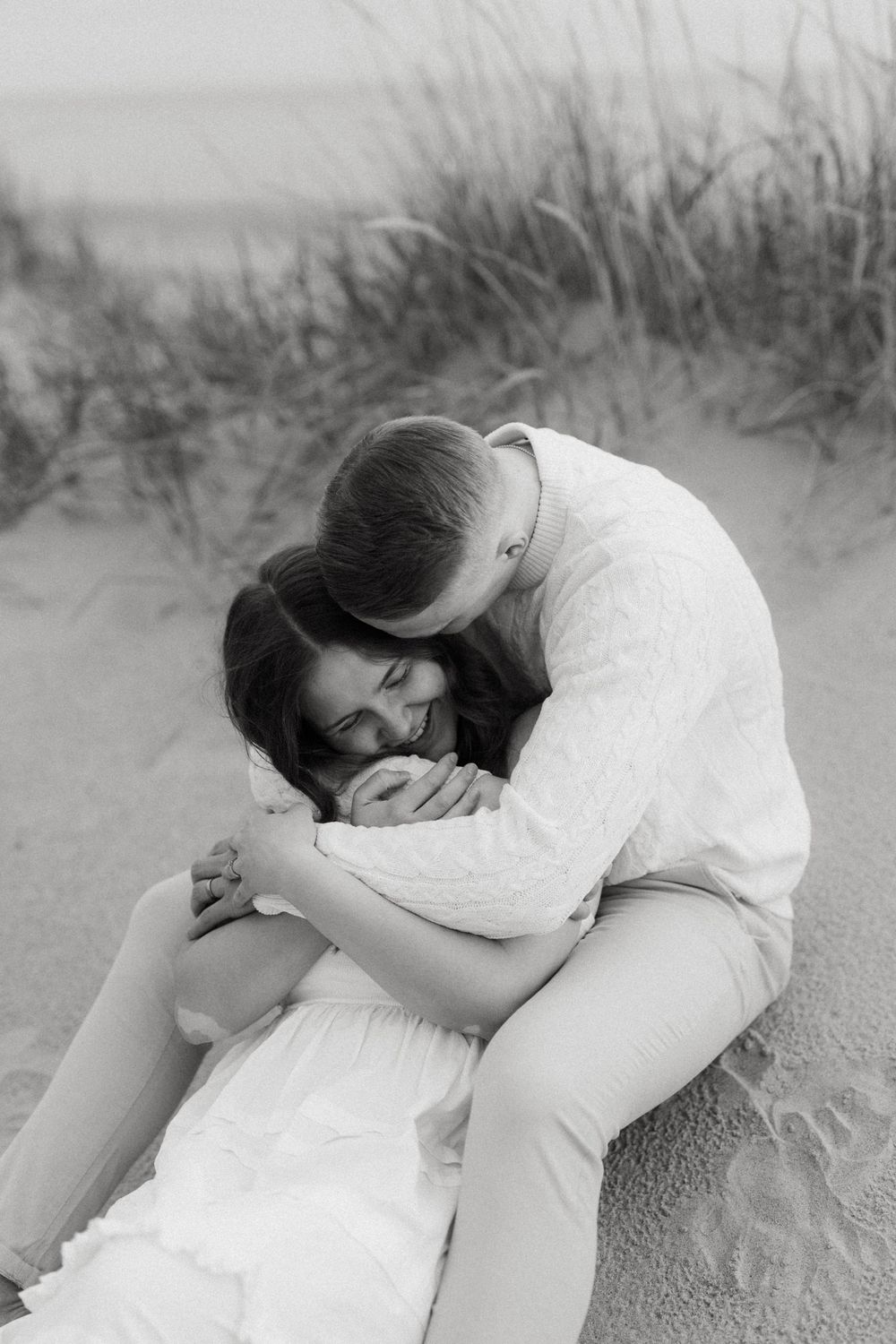 A series of black and white photos showing someone in white clothing lying curled up on sandy ground near beach grass.