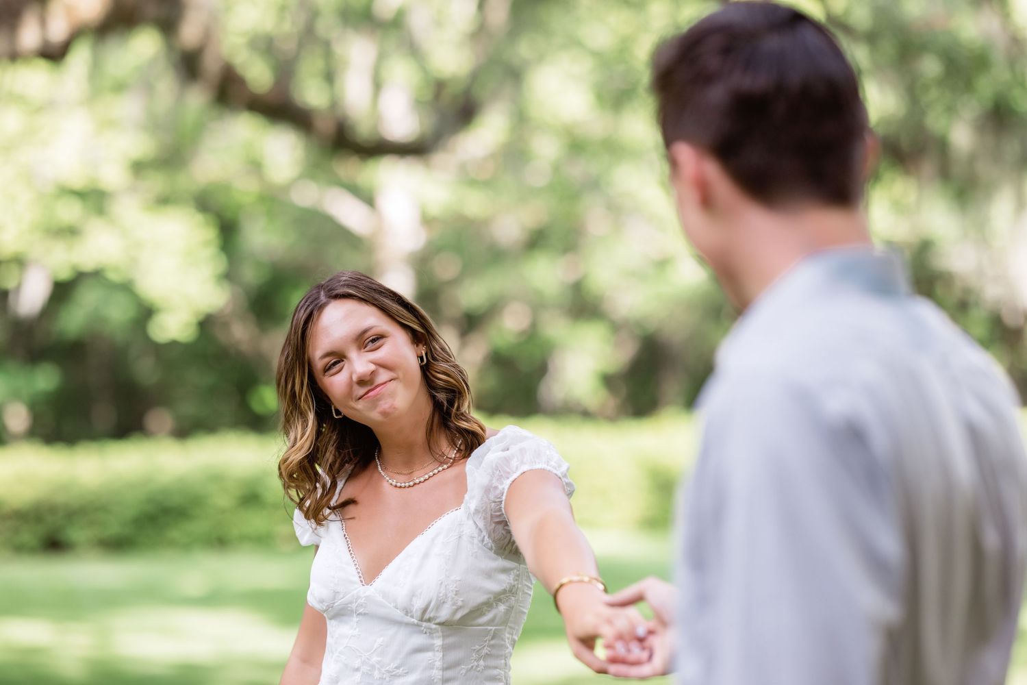 Romantic outdoor scene shows a couple in wedding attire laughing together in a sun-dappled garden setting.