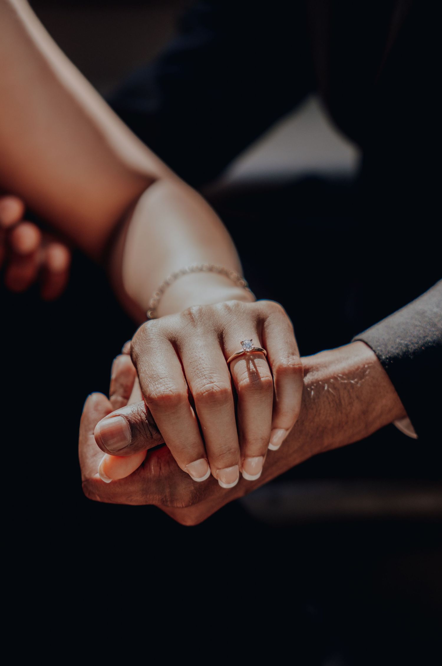 Close-up of two hands holding together, one with a tattoo and an engagement ring.