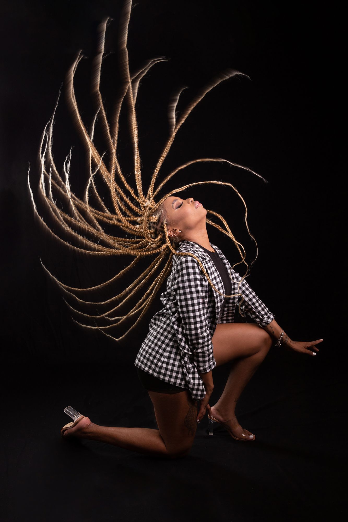 Dynamic dancer in checkered shirt flips hair in dramatic motion against dark background during expressive performance.