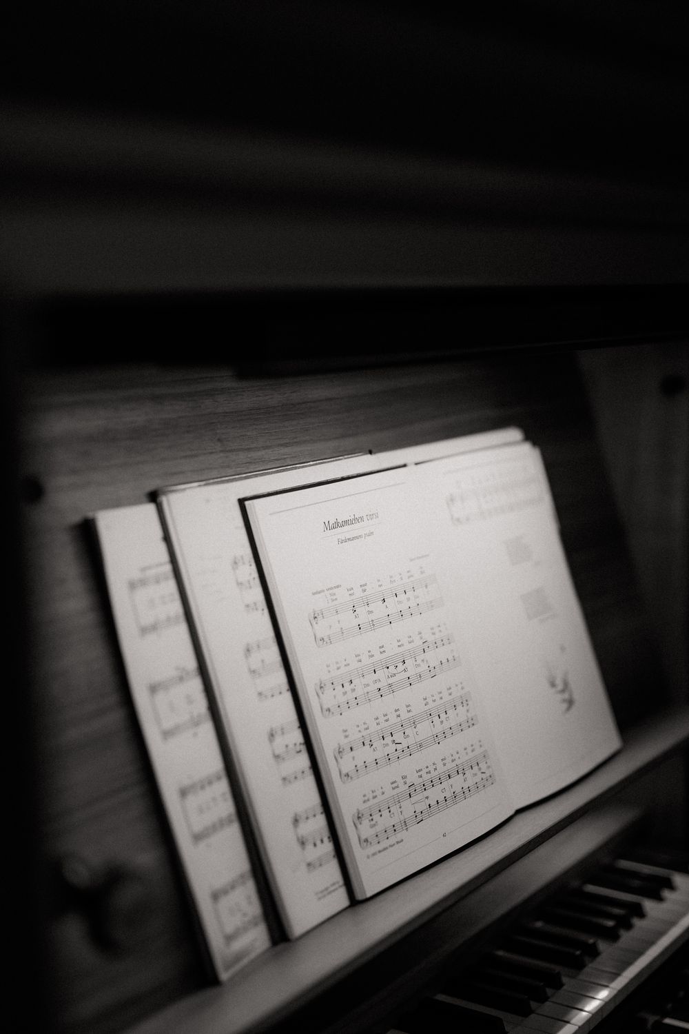 Black and white photo of sheet music on a piano music stand with piano keys visible in the foreground.