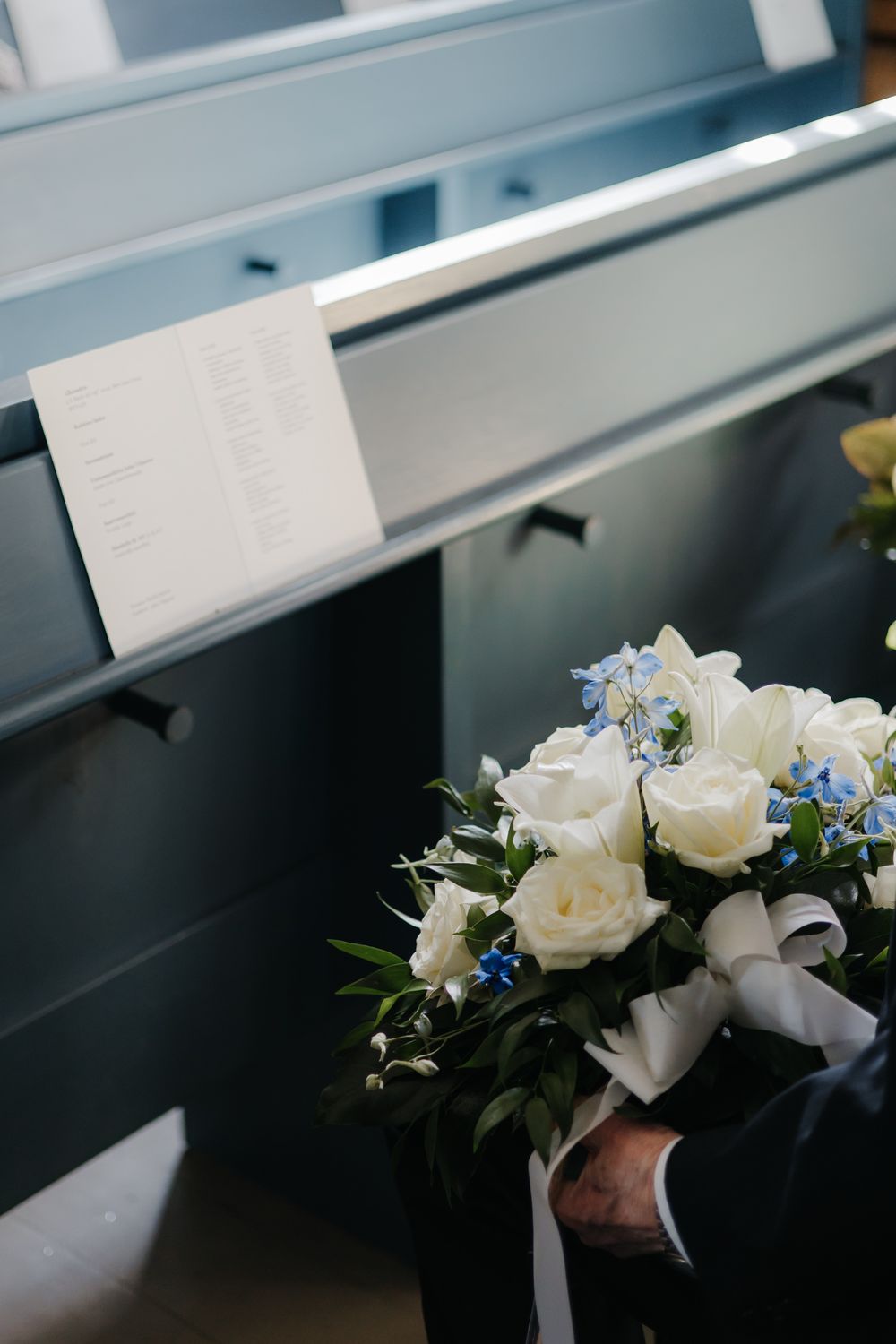 White roses and delicate blue flowers arranged in an elegant corsage with satin ribbon against a dark background.