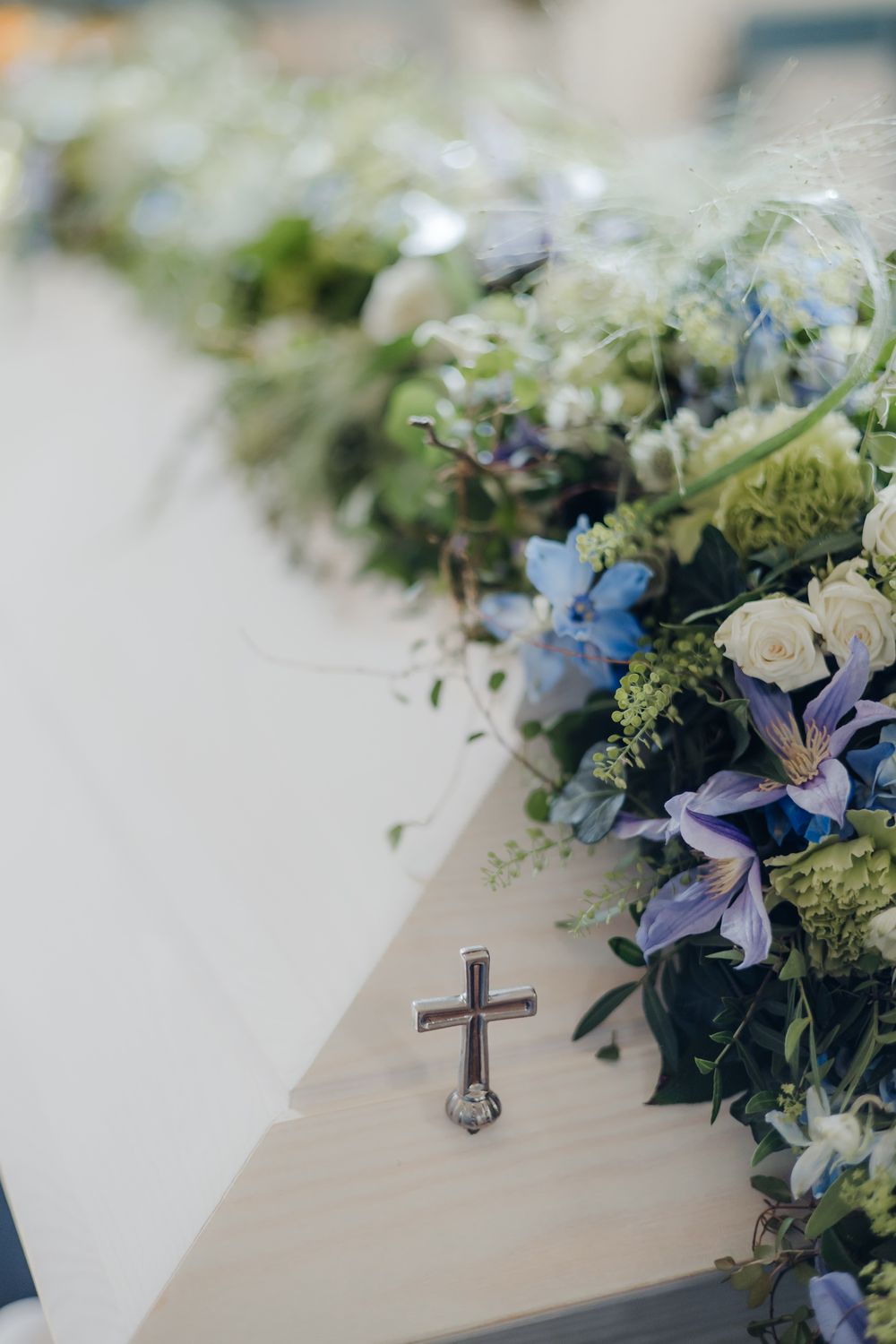 Delicate blue and white floral wedding decorations with greenery arranged on a light colored surface.