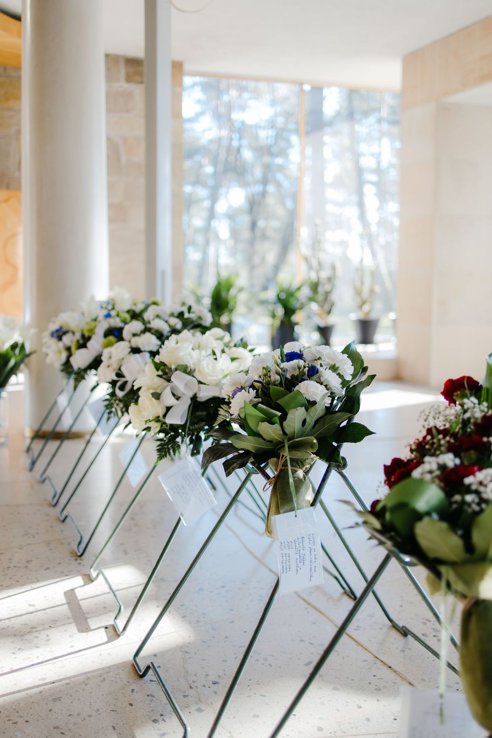 White floral arrangements with name cards displayed in a row along a bright windowsill for an elegant event setup.