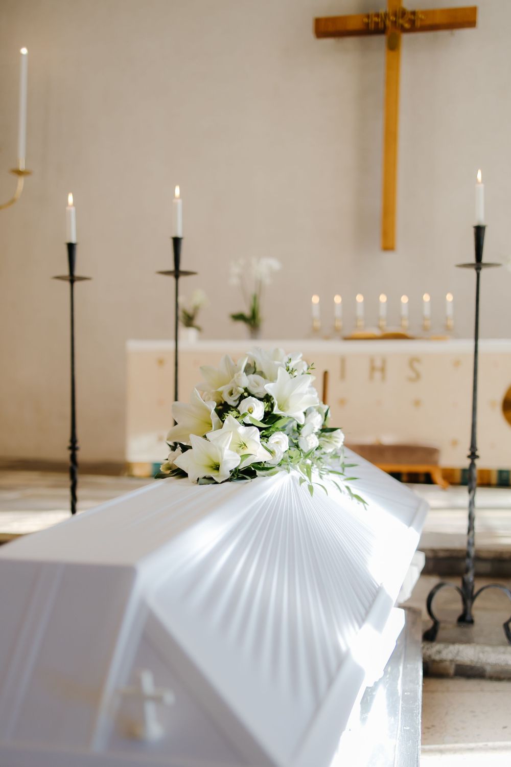 White draped casket with floral arrangements and black candelabras in a church setting.