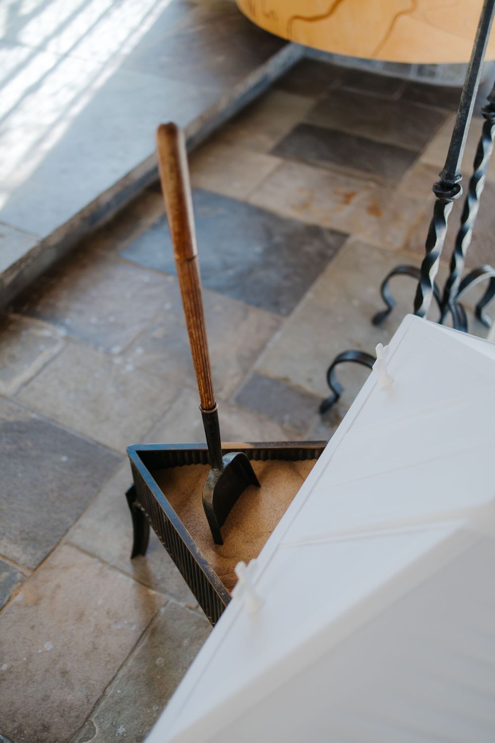 A black broom with wooden handle rests against a white wall on stone tile flooring.