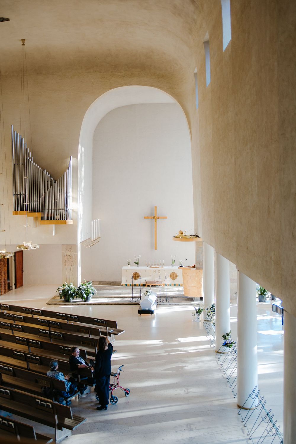 Interior view of a modern minimalist church sanctuary with wooden pews and white arched walls bathed in natural light.
