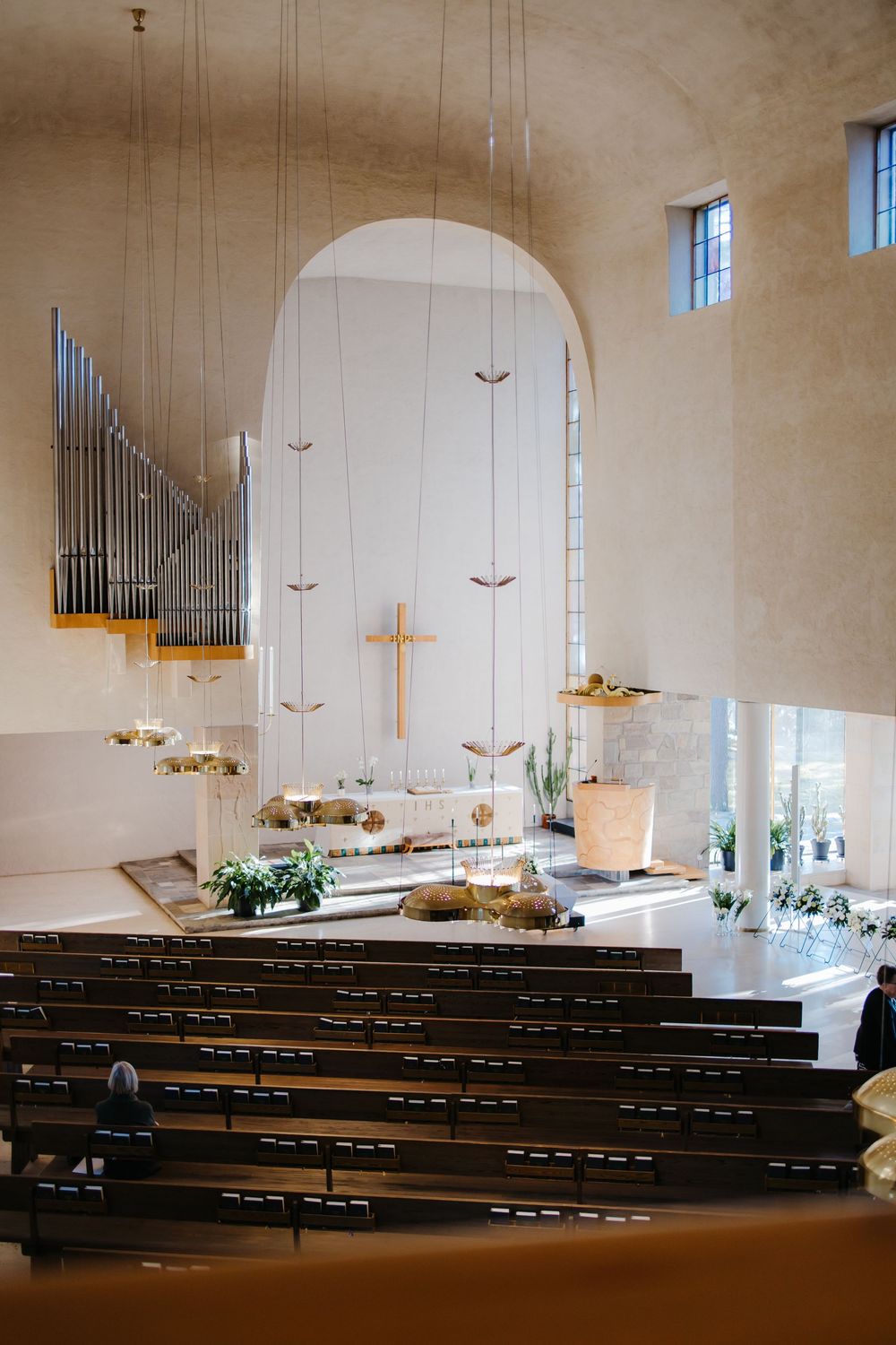 Panoramic view of a modern church interior with wooden pews and a golden cross at the altar.