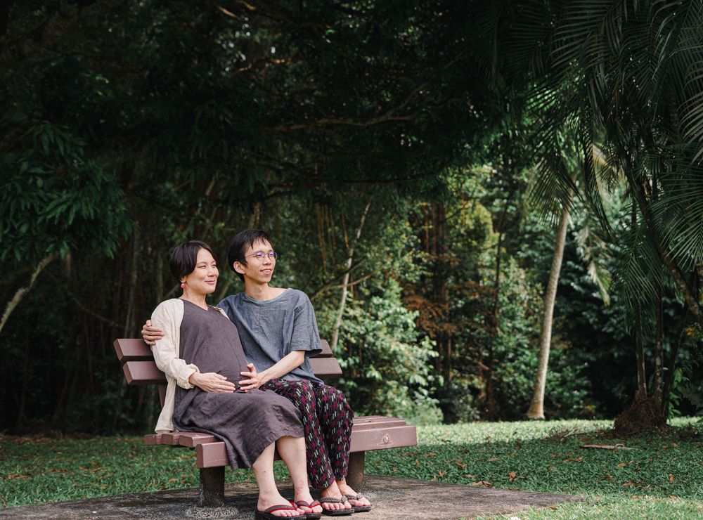 Two people sitting together on a wooden bench in a lush garden setting.