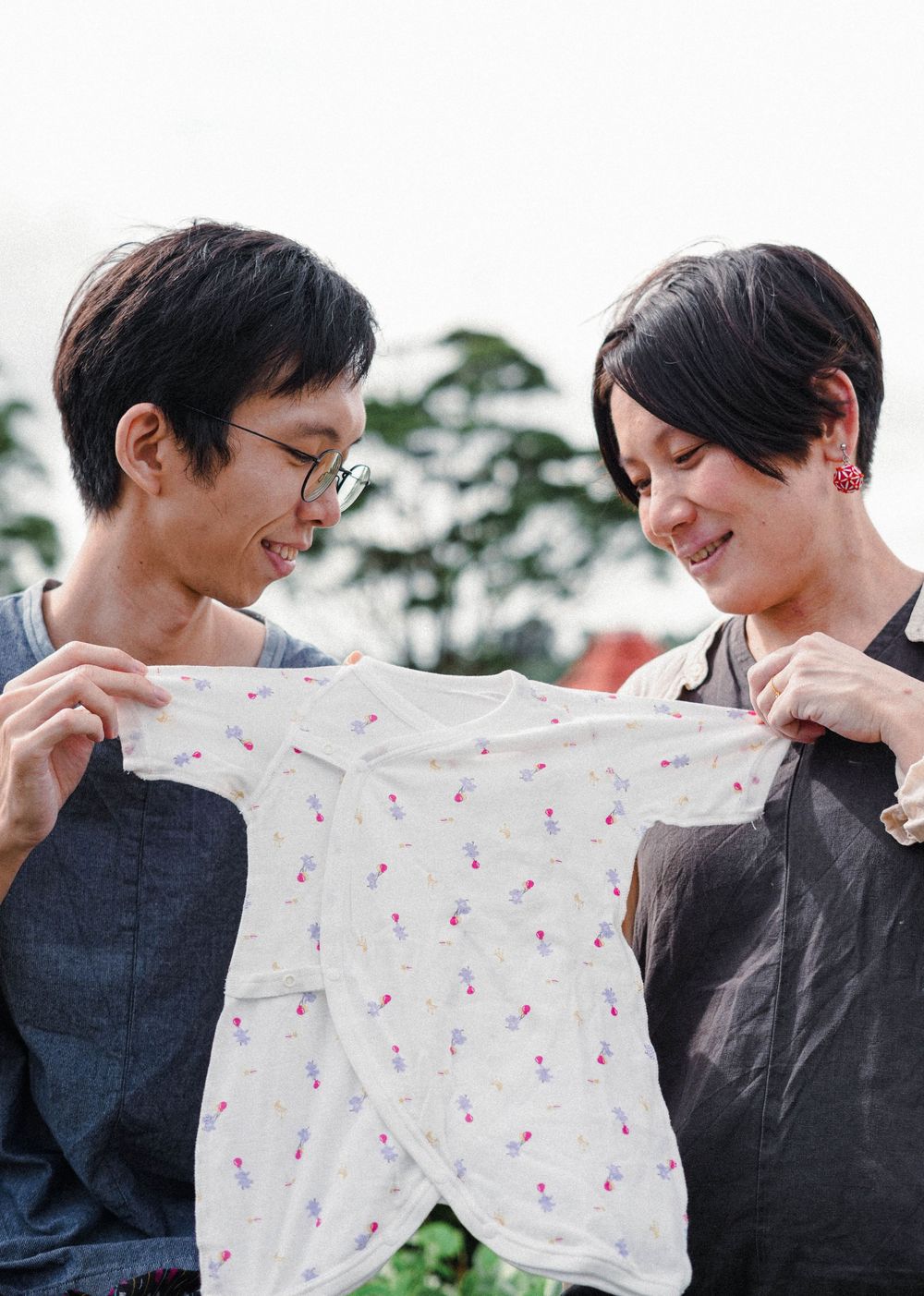 Two people hold and admire a small floral patterned baby garment together outdoors.