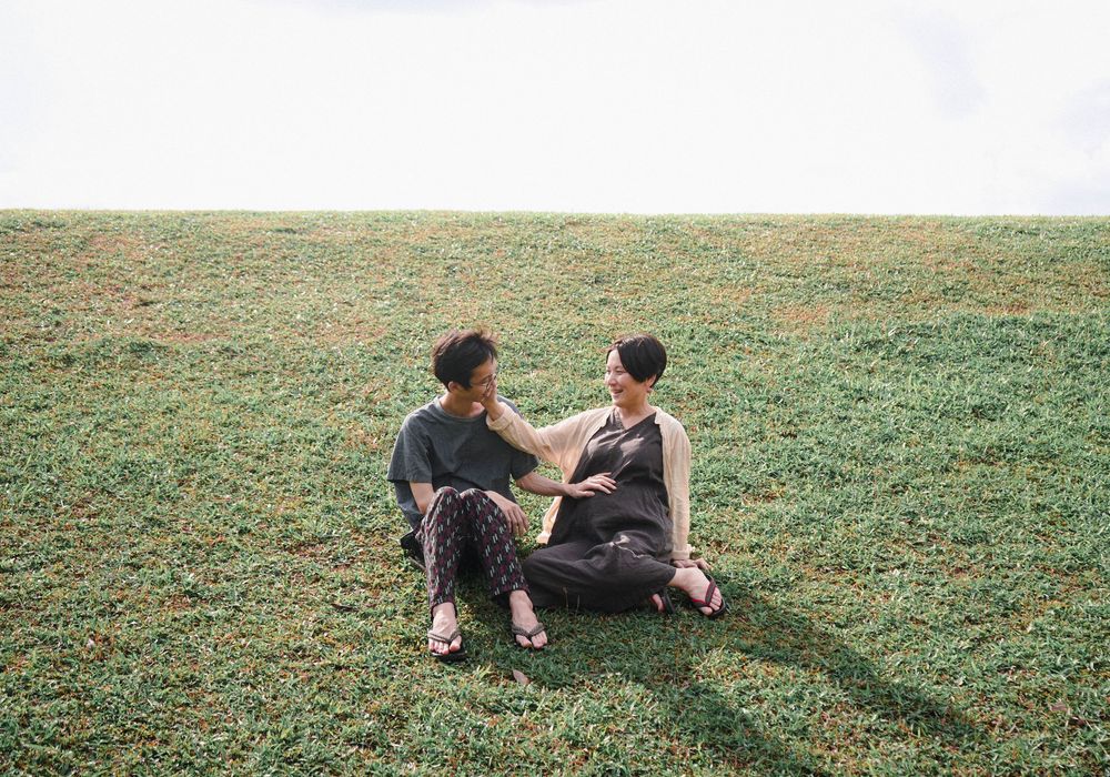 Two people sit close together and chat while relaxing on a grassy hillside slope on a sunny day.