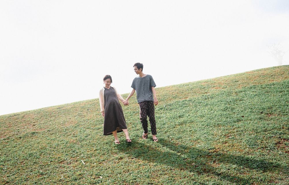 Two figures walk together on a grassy hillside slope on a bright sunny day casting long shadows behind them.