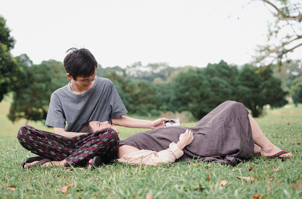 A couple relaxing together on grass in a park, with one person sitting while the other lies down.