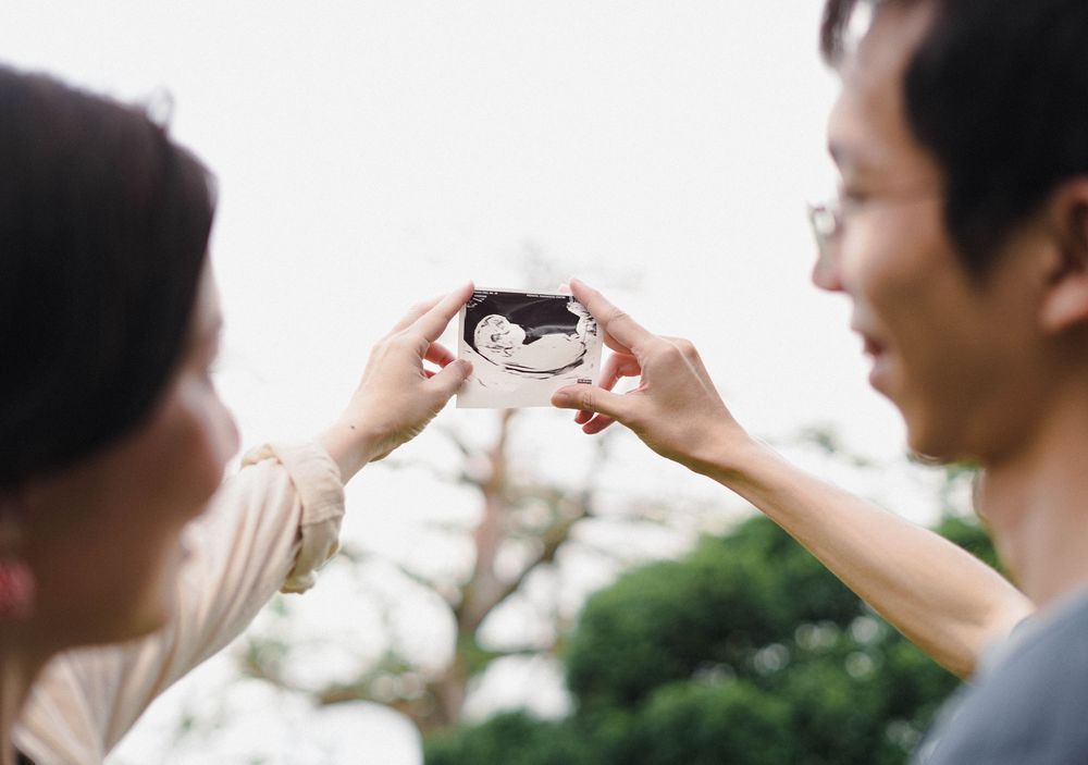 Two people sharing a smartphone displaying a sonogram photo outdoors on a bright day.