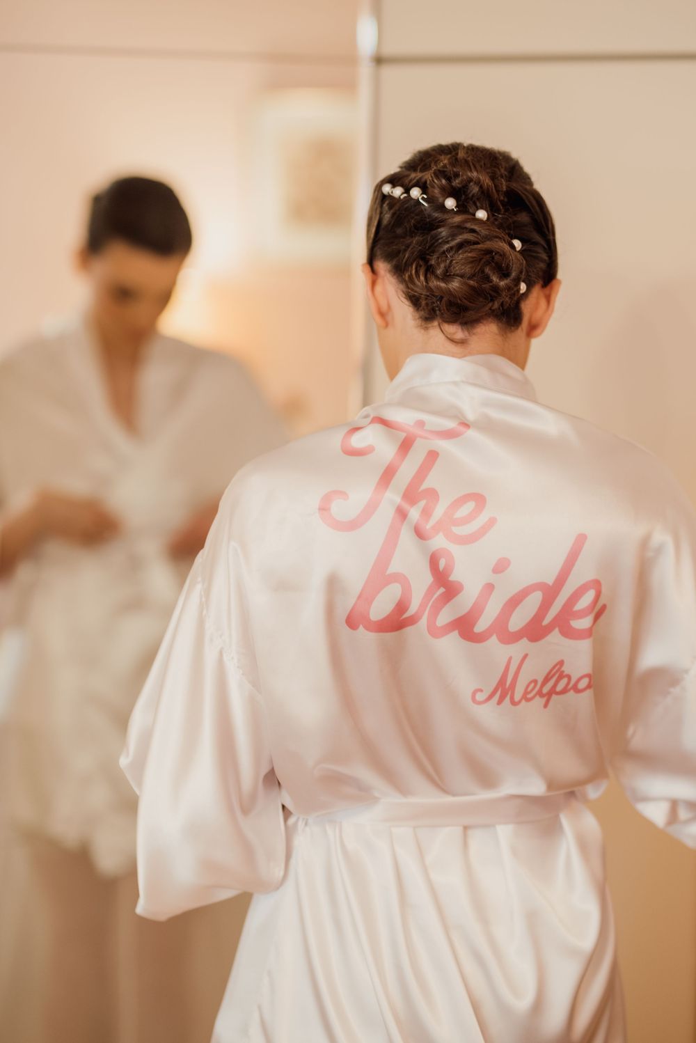 A white satin robe with 'The bride' embroidered in pink text is shown from behind.