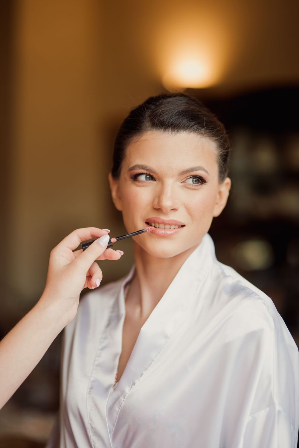 Close up of bridal makeup application showing lip color being applied in warm lighting.
