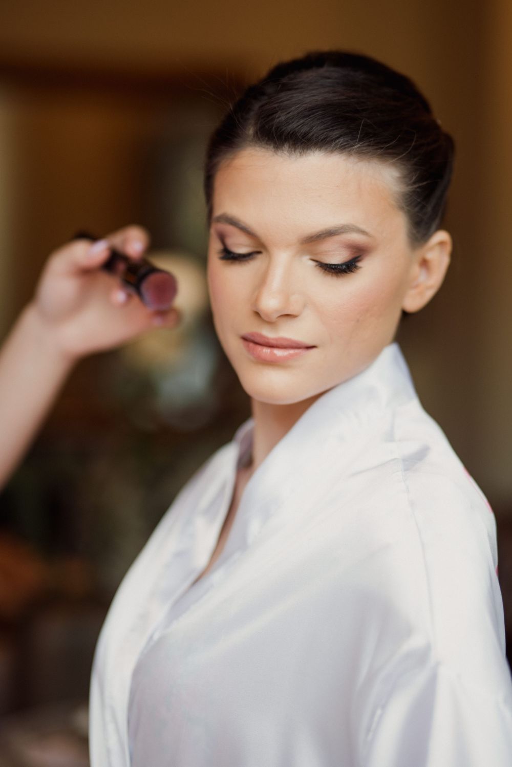 A person in a white robe getting makeup applied during wedding preparations.