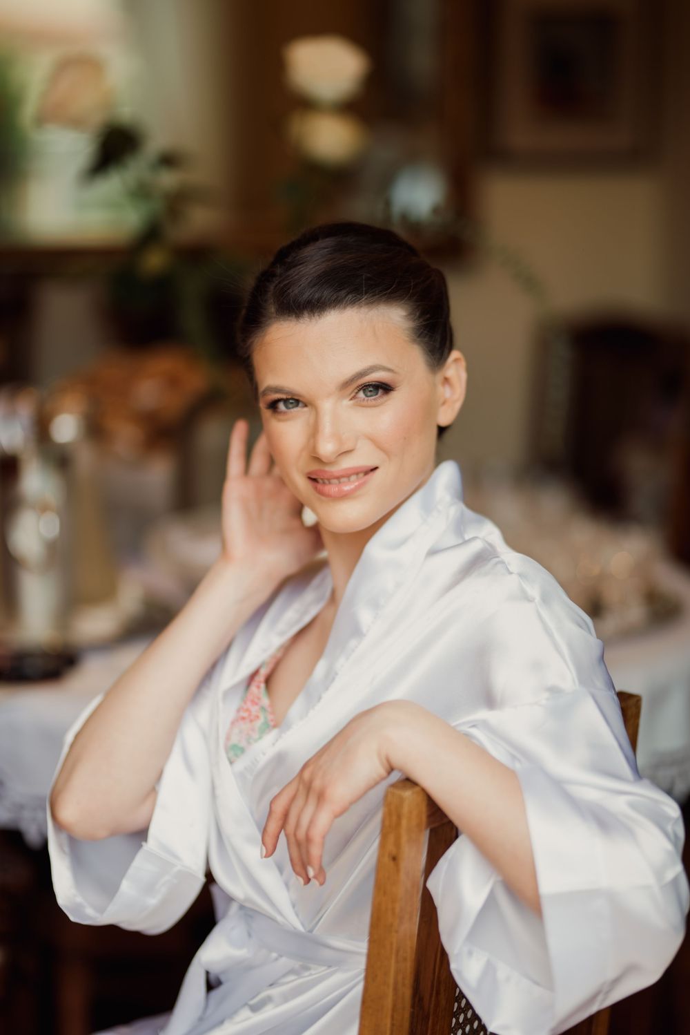 Relaxed posed portrait of woman in white robe resting arm on wooden chair.