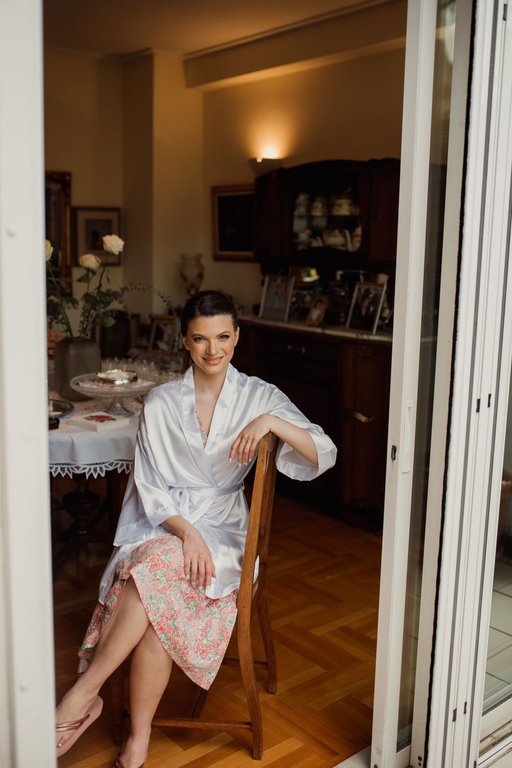 Full length view of woman in white robe sitting elegantly in doorway with vintage decor.