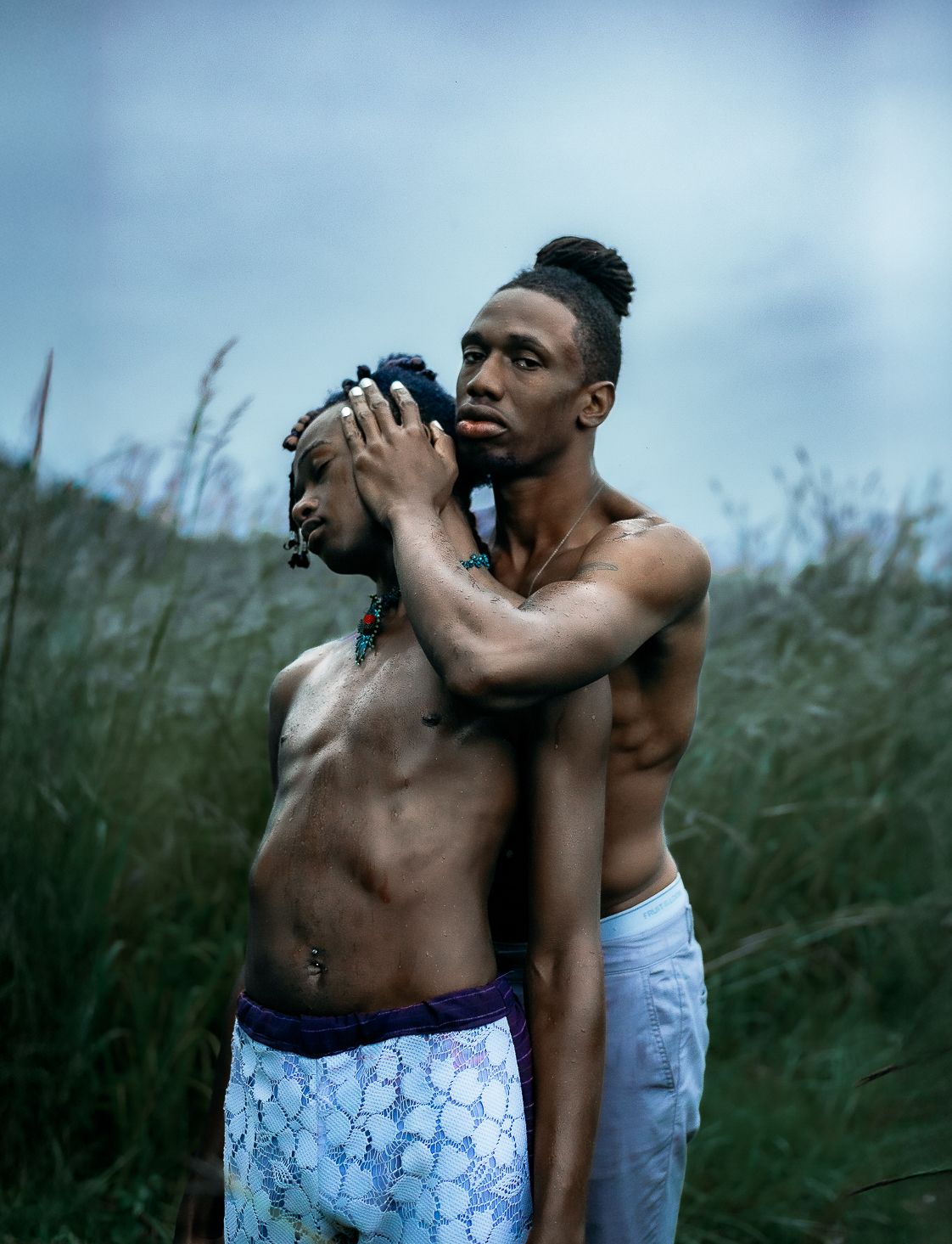 A series of artistic photos showing two people embracing in tall grass against a moody blue sky.