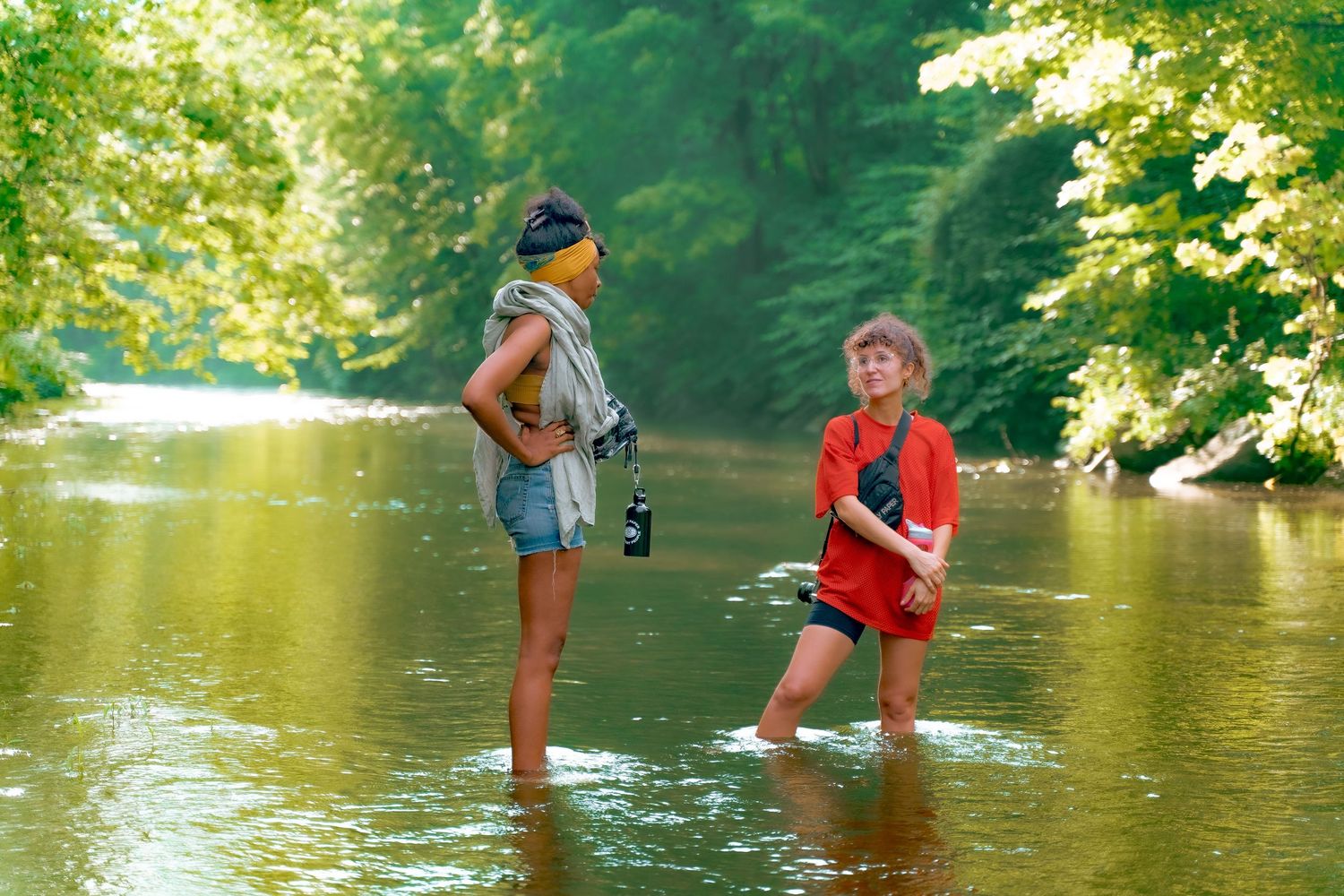 Two people wading and playing in a peaceful forest stream on sunny day.