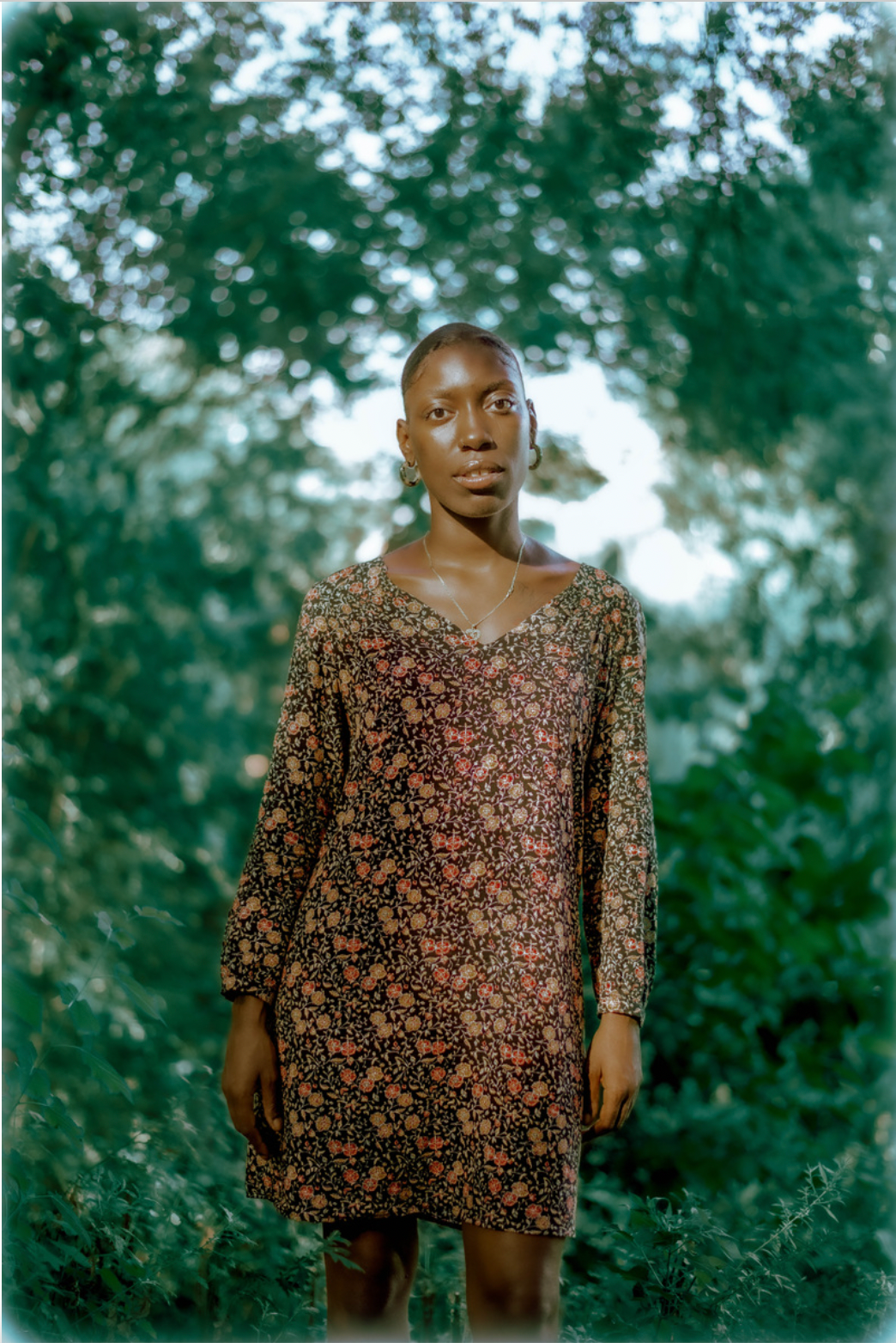 Portrait of person in floral dress standing against green foliage background.