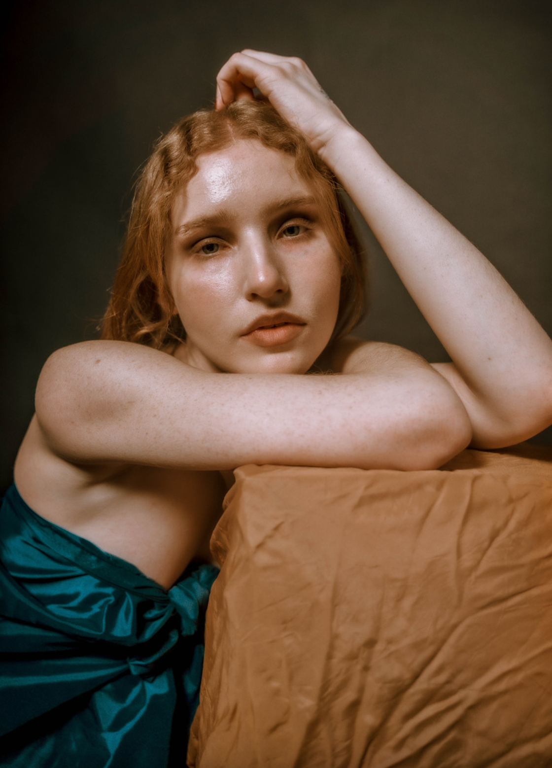 Artistic portrait with subject leaning on brown cushion in emerald dress.