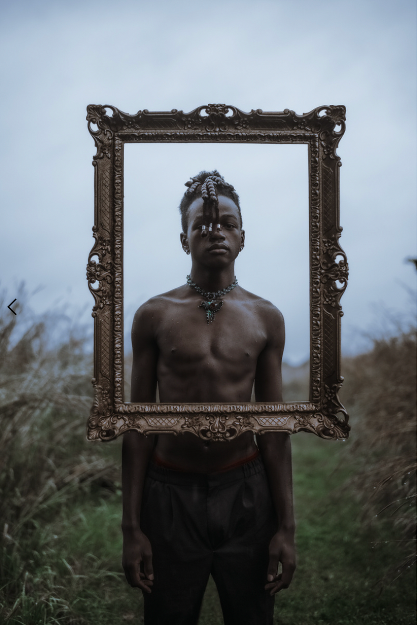 Figure framed by ornate gold frame standing in natural outdoor setting.