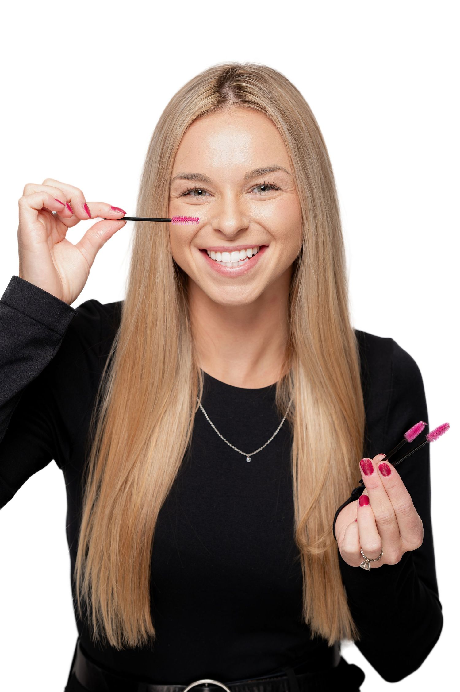 Young woman in black sweater smiling while holding pink mascara wand and tube against white background.