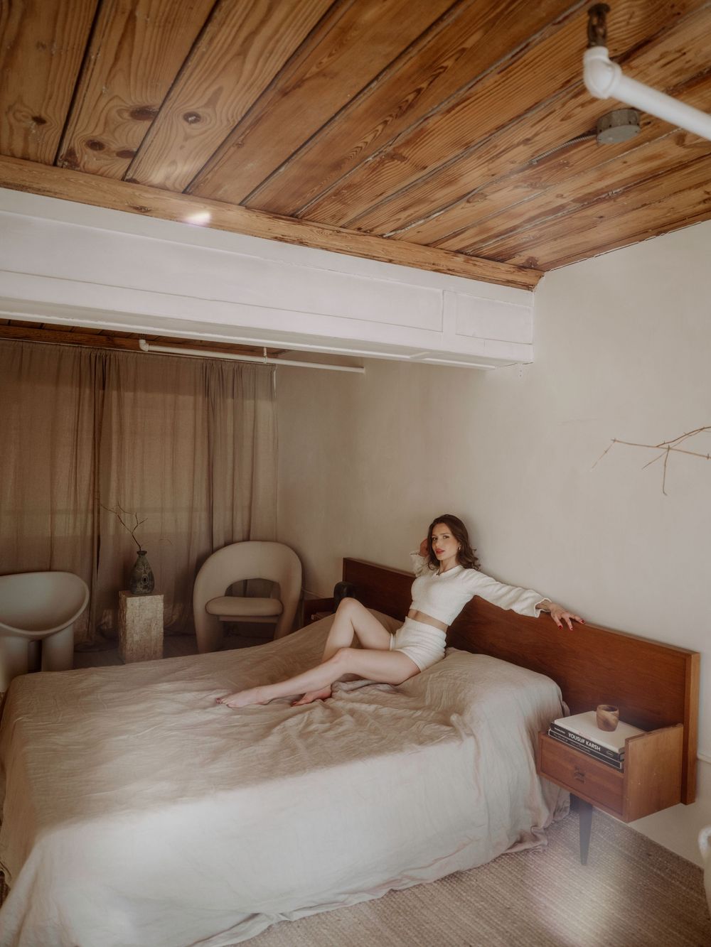 Cozy bedroom interior with wooden ceiling, white walls, and a bed with warm lighting and earth-toned decor.