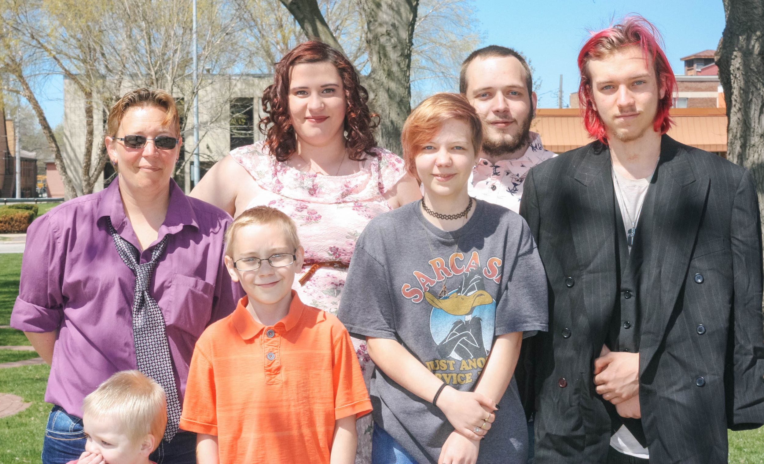 Family group poses together outdoors in front of trees on a bright spring day.